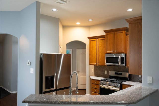 kitchen with arched walkways, stainless steel appliances, visible vents, and decorative backsplash