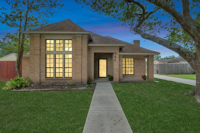 view of front facade featuring brick siding, a shingled roof, a front lawn, and fence