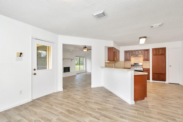 kitchen featuring wood finish floors, stainless steel range oven, brown cabinets, and visible vents