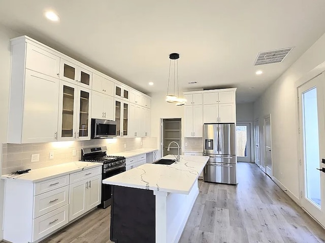 kitchen featuring appliances with stainless steel finishes, sink, white cabinets, hanging light fixtures, and a kitchen island with sink