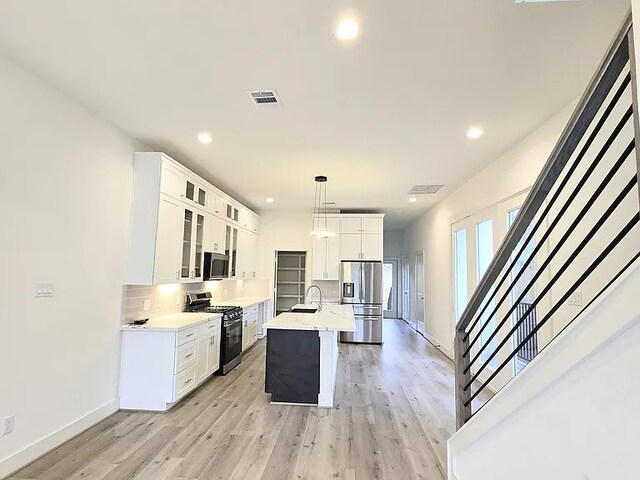 kitchen featuring sink, decorative light fixtures, a center island with sink, appliances with stainless steel finishes, and white cabinets