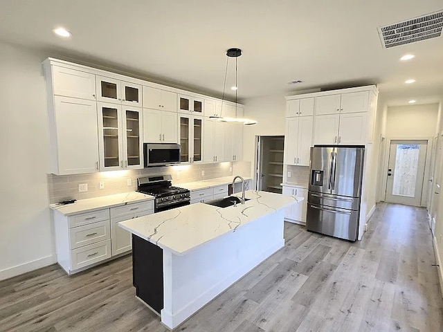 kitchen with sink, white cabinetry, decorative light fixtures, a center island with sink, and stainless steel appliances