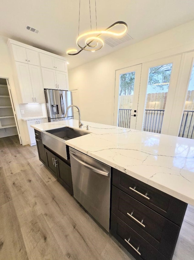 kitchen with appliances with stainless steel finishes, sink, white cabinets, hanging light fixtures, and light hardwood / wood-style flooring