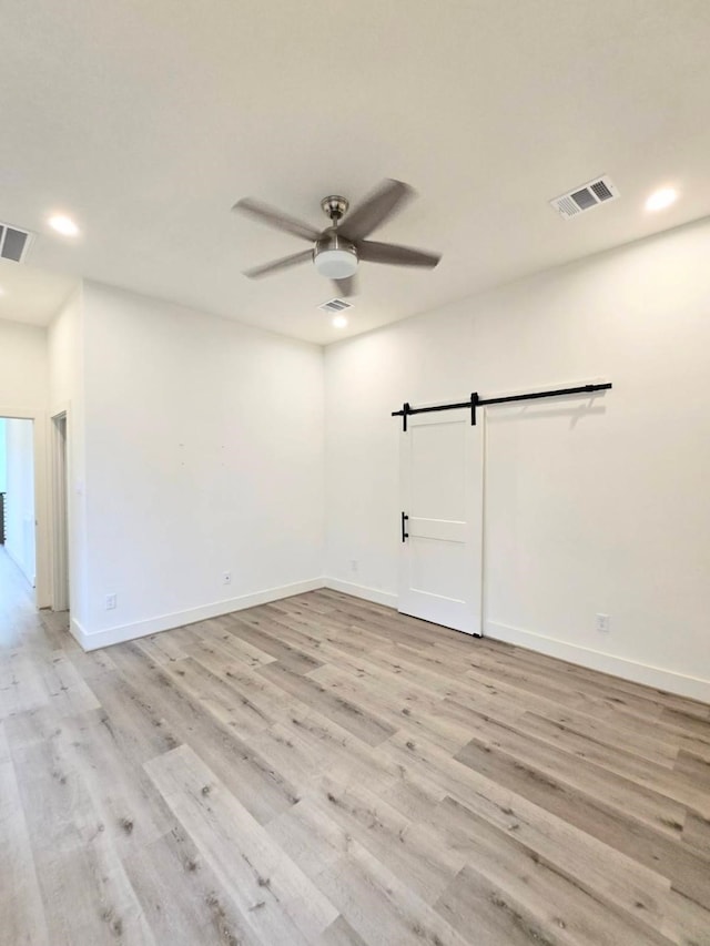 spare room featuring a barn door, ceiling fan, and light wood-type flooring