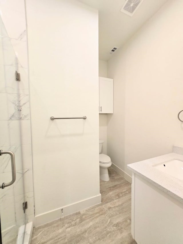 bathroom featuring vanity, wood-type flooring, a shower with shower door, and toilet