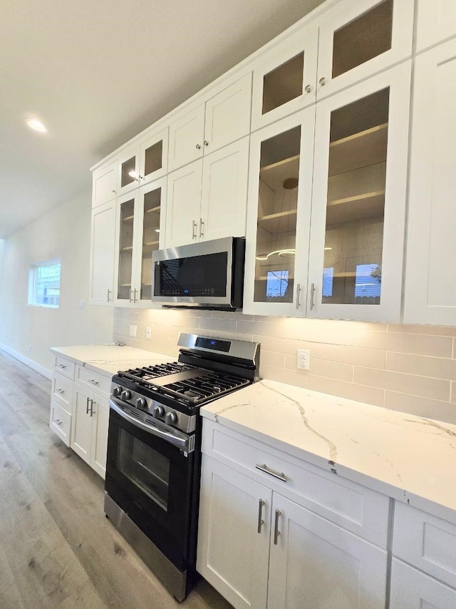 kitchen featuring stainless steel appliances, tasteful backsplash, light stone countertops, and white cabinets