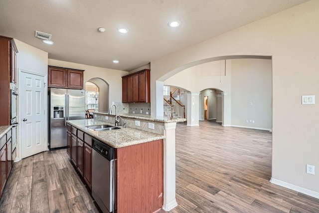 kitchen with sink, hardwood / wood-style flooring, appliances with stainless steel finishes, light stone countertops, and an island with sink