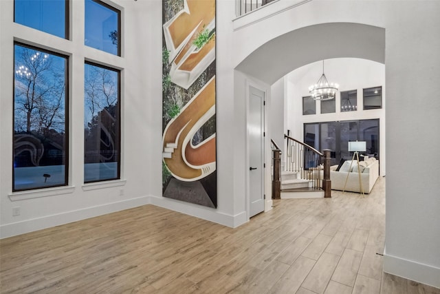 interior space featuring a towering ceiling, stairway, a chandelier, and wood finished floors