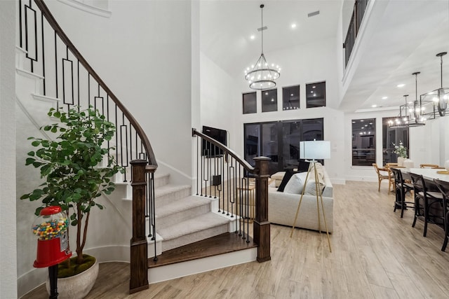 entryway with a high ceiling, visible vents, stairs, light wood-type flooring, and an inviting chandelier