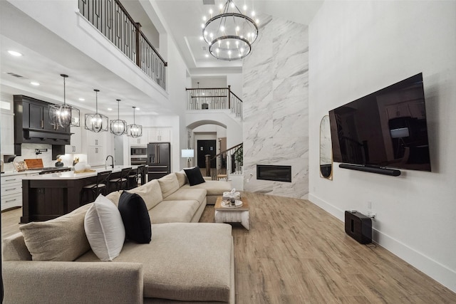 living room with a high ceiling, a premium fireplace, baseboards, light wood finished floors, and an inviting chandelier