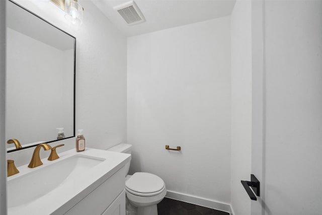 half bathroom with toilet, vanity, visible vents, and baseboards