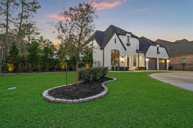 french country home with a yard, driveway, an attached garage, and stucco siding