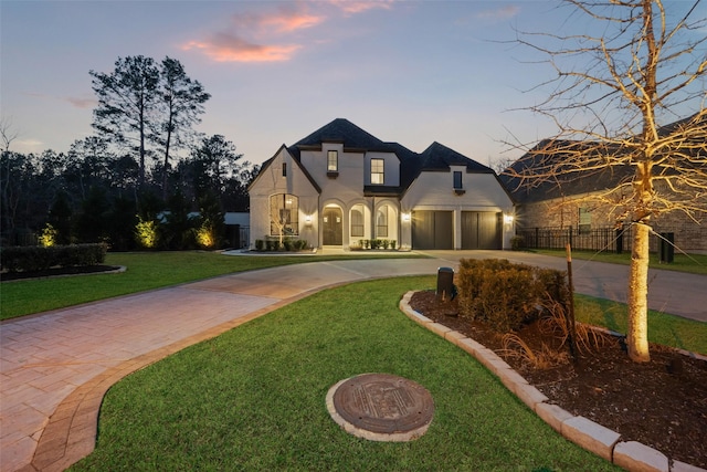 french country style house with a yard, fence, driveway, and stucco siding