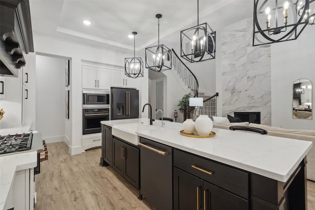 kitchen featuring a center island with sink, white cabinets, light wood-style flooring, black appliances, and a sink