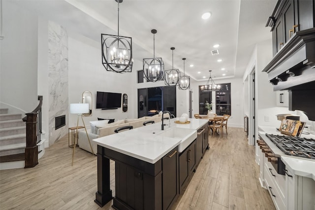 kitchen with a fireplace, light countertops, light wood-style floors, a kitchen island with sink, and a sink