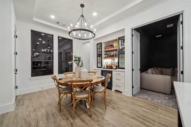 dining room featuring a dry bar, light wood finished floors, beverage cooler, visible vents, and a raised ceiling