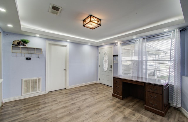 home office with built in desk, light hardwood / wood-style floors, and a tray ceiling