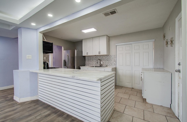 kitchen featuring sink, white cabinetry, stainless steel refrigerator with ice dispenser, tasteful backsplash, and kitchen peninsula