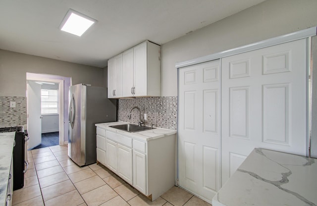 kitchen featuring appliances with stainless steel finishes, tasteful backsplash, sink, white cabinets, and light tile patterned floors