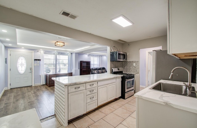 kitchen featuring sink, appliances with stainless steel finishes, a raised ceiling, white cabinets, and backsplash