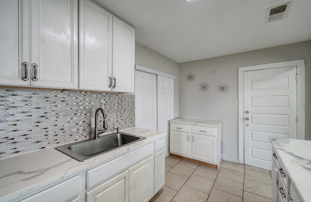 kitchen with light tile patterned flooring, sink, white cabinetry, light stone countertops, and backsplash