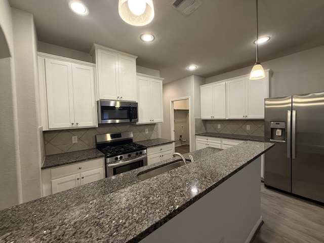 kitchen with sink, white cabinetry, decorative light fixtures, appliances with stainless steel finishes, and dark stone counters