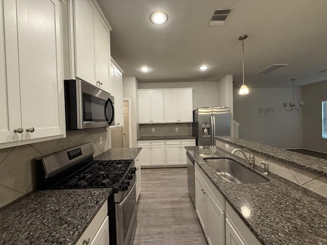 kitchen featuring sink, decorative light fixtures, dark stone countertops, stainless steel appliances, and white cabinets