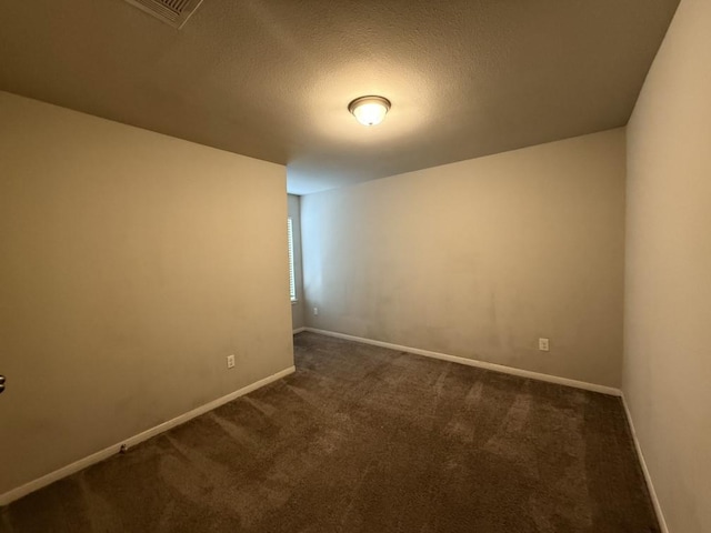 spare room featuring dark carpet and a textured ceiling