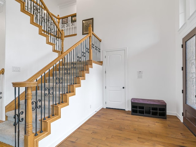 stairway with wood-type flooring, a towering ceiling, and ornamental molding