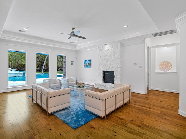 living room featuring ornamental molding, hardwood / wood-style floors, a fireplace, and a tray ceiling