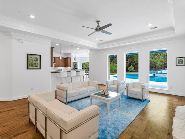 living room featuring a raised ceiling, wood-type flooring, and crown molding