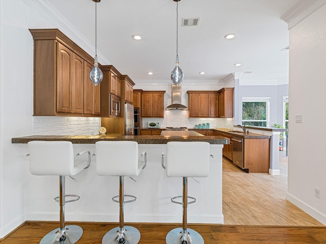 kitchen featuring wall chimney exhaust hood, a breakfast bar area, decorative light fixtures, kitchen peninsula, and stainless steel appliances