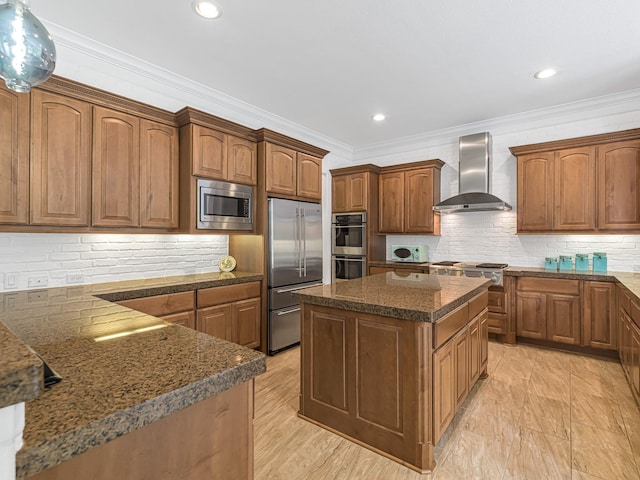 kitchen featuring wall chimney range hood, crown molding, a center island, built in appliances, and decorative backsplash