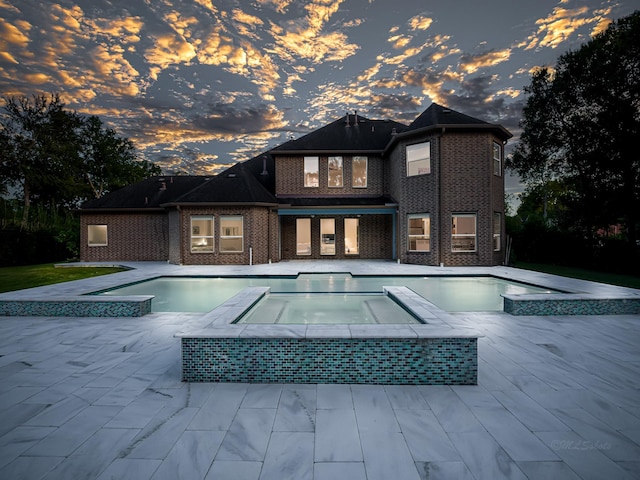 pool at dusk featuring an in ground hot tub and a patio