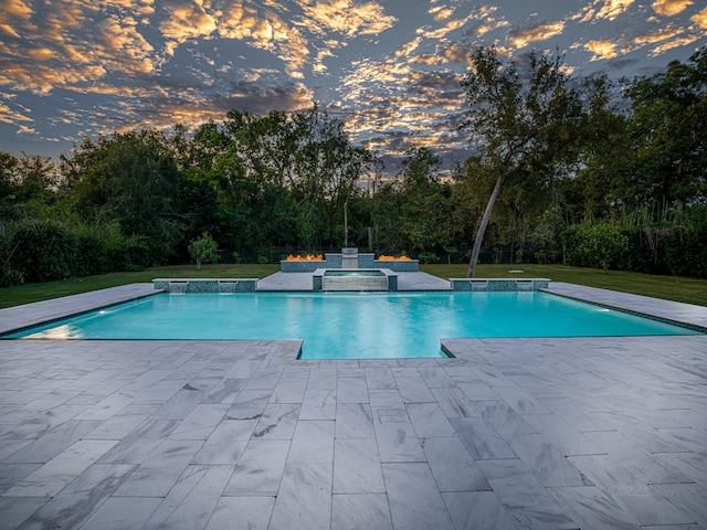 pool at dusk featuring an in ground hot tub, a yard, and a patio area