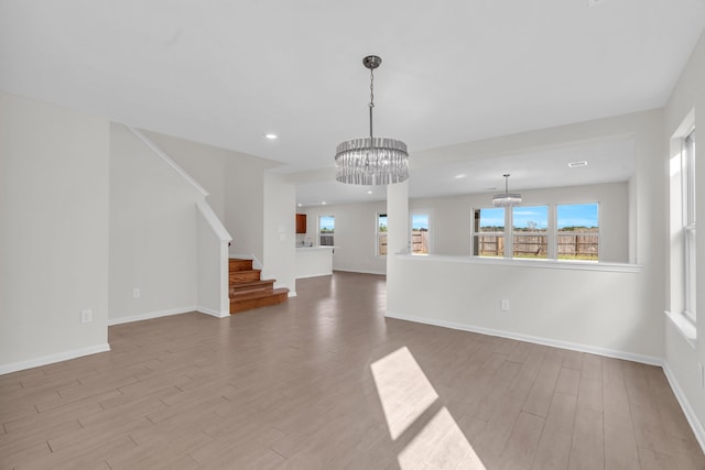 unfurnished living room featuring plenty of natural light, a chandelier, and light wood-type flooring