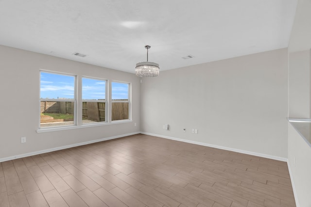 spare room featuring an inviting chandelier and light hardwood / wood-style flooring