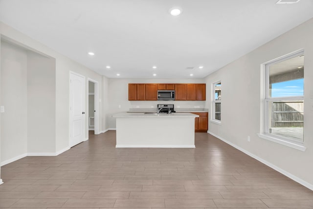 kitchen featuring stainless steel appliances, light hardwood / wood-style floors, and a center island with sink