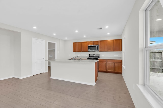 kitchen featuring appliances with stainless steel finishes, a kitchen island with sink, sink, and light wood-type flooring