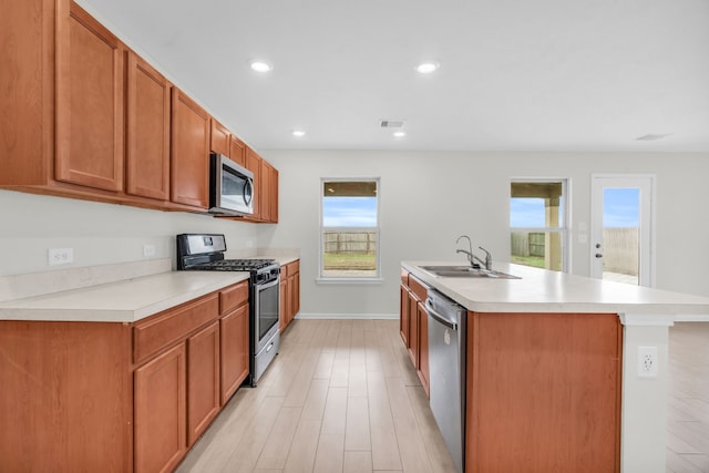 kitchen featuring appliances with stainless steel finishes, light hardwood / wood-style floors, sink, and a center island with sink