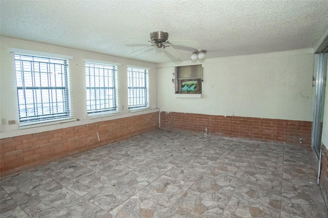 unfurnished room featuring ceiling fan, brick wall, and a textured ceiling