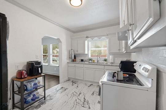 kitchen featuring tasteful backsplash, sink, white cabinets, ornamental molding, and electric stove