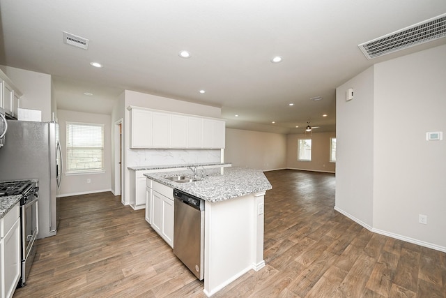 kitchen featuring hardwood / wood-style flooring, a kitchen island with sink, stainless steel appliances, light stone counters, and white cabinets