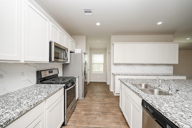 kitchen featuring appliances with stainless steel finishes, white cabinetry, sink, light stone counters, and light wood-type flooring