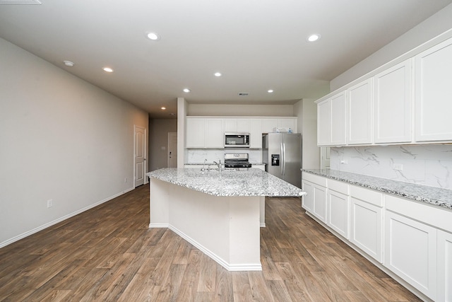 kitchen featuring light stone counters, stainless steel appliances, an island with sink, and white cabinets