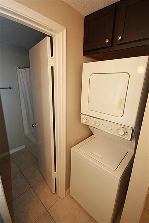 laundry room featuring light tile patterned flooring, stacked washer / dryer, and a textured ceiling