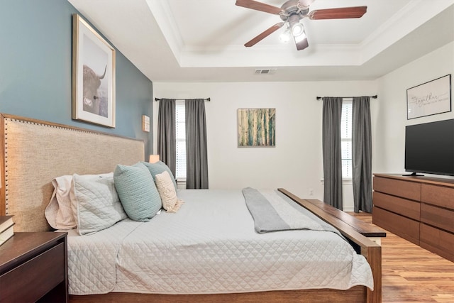 bedroom featuring ornamental molding, wood-type flooring, ceiling fan, and a tray ceiling