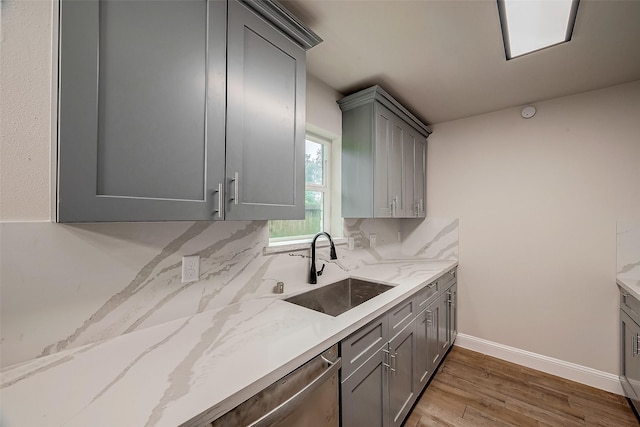 kitchen with sink, light wood-type flooring, gray cabinets, light stone countertops, and backsplash