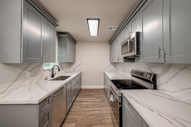 kitchen with gray cabinets, tasteful backsplash, sink, stainless steel appliances, and light stone countertops