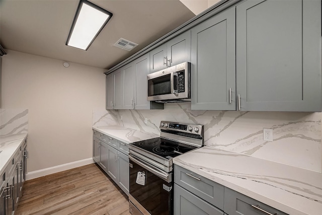 kitchen with light stone counters, appliances with stainless steel finishes, tasteful backsplash, and gray cabinetry